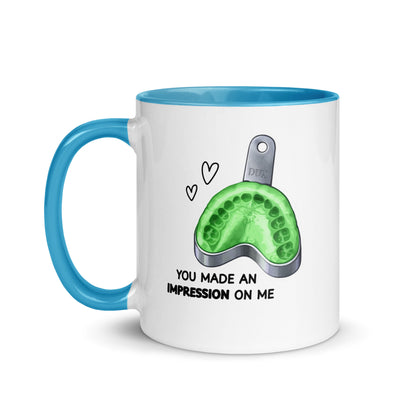 Weiße Keramiktasse mit farbigem Henkel und Innenseite sowie Abdrucklöffel-Motiv mit grünem Abformmaterial und Schriftzug „You made an impression on me“ – humorvolle Dental-Tasse für Zahnmedizin und Kieferorthopädie