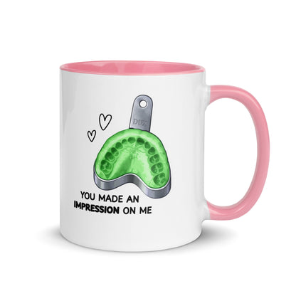 Weiße Keramiktasse mit farbigem Henkel und Innenseite sowie Abdrucklöffel-Motiv mit grünem Abformmaterial und Schriftzug „You made an impression on me“ – humorvolle Dental-Tasse für Zahnmedizin und Kieferorthopädie